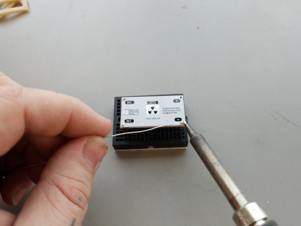 A hand holds a soldering iron in position to solder the pins in place on a white PCB