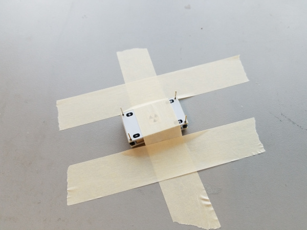 The PCB on the top of the stack has been taped down to the workbench using masking tape to apply clamping force to the stack.