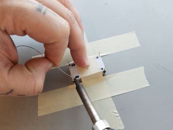 A hand holds a soldering iron in position to solder the pins