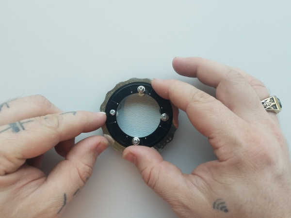Two hands hold the LED ring, now in position on top of the stack with LEDs facing down.
