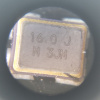 Microscope detail of a 4 pin part that also appears to be a crystal resonator labeled 16.0 J M 3JM