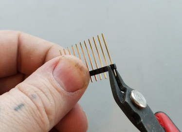 A hand holds a strip of pin headers while snipping one away using wire snips