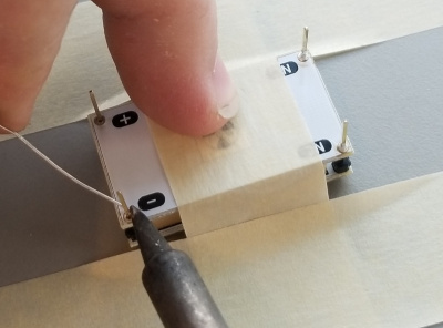 A hand holds a soldering iron in position to solder the pins