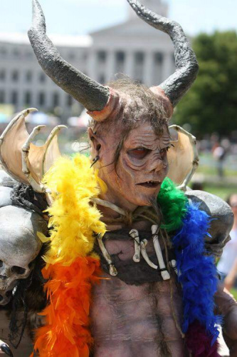 intimidatingly costumed person wearing a rainbow-colored feather boa