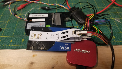 A card reader module rests on the workbench alongside a saleae logic analyzer which is connected to a stack of objects taped together. From bottom to top, the stack is a VISA debit card, a shim shim board, the skimmer board and another shim shim board.