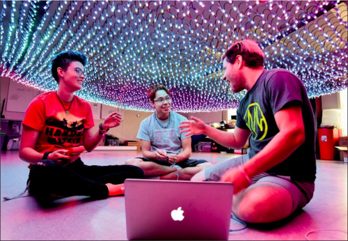 Mariah sitting under a net of LED lights with two others