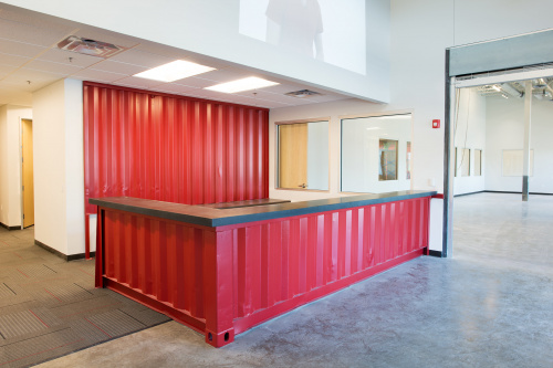 A red reception desk and backdrop both cut from a corrugated shipping container.