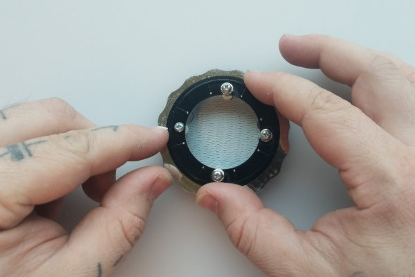 Two hands hold the LED ring, now in position on top of the stack with LEDs facing down.